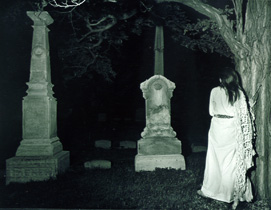Cemetery at night, eeriely woman stands by a tree